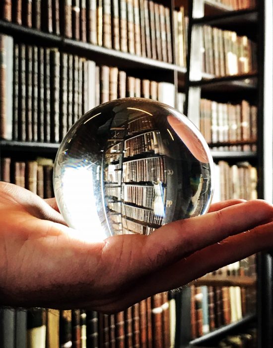 glass-ball-in-hand-and-old-book-shelves-in-the-bac-VG5TTXJ